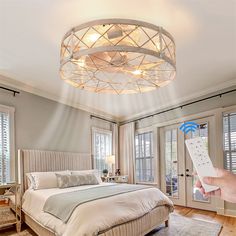 a person holding a remote control in front of a bed with a circular light fixture