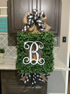 a monogrammed boxwood wreath with the letter b is displayed on a kitchen counter