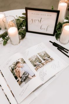 an open book sitting on top of a white table next to candles and greenery