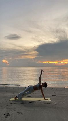 a woman is doing yoga on the beach at sunset with her arms in the air