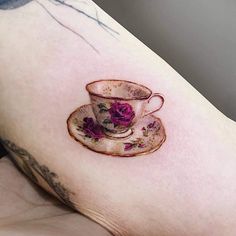 a cup and saucer tattoo on the right side of the left arm, with pink flowers in it