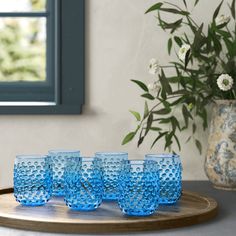 five blue glasses sitting on top of a wooden tray next to a potted plant