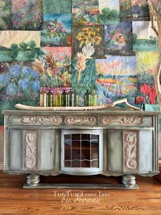 an old dresser with flowers and vases on it in front of a colorful wall