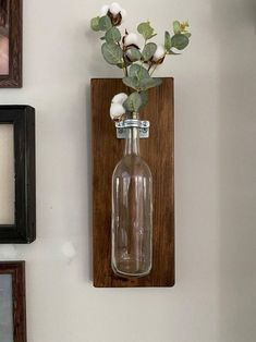 there is a bottle with flowers in it hanging on the wall next to framed pictures