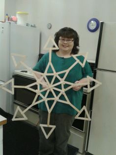 a woman standing in front of a refrigerator holding a wooden snowflake that has been cut out