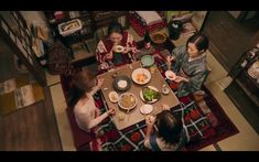 three women sitting at a table with food in front of them, looking down on the floor