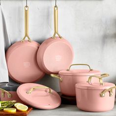 pink pots and pans hanging from hooks in a kitchen with lemon slices on the counter