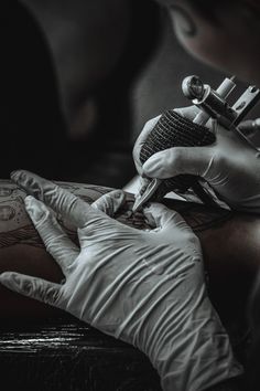 a person getting their tattoo done by someone with white gloves and tattoos on his arm