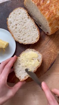 a person cutting bread on top of a wooden cutting board with butter in front of them