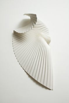 an abstract white paper sculpture on a white surface, with the shape shaped like a shell