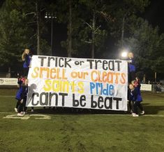 some cheerleaders holding up a sign on the sidelines at night with trees in the background