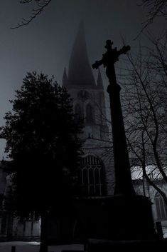 a black and white photo of a cross in front of a church at night with fog