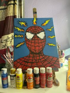 a spiderman painting on an easel surrounded by paints