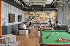 people are playing pool in an industrial style room with graffiti on the walls and wood flooring