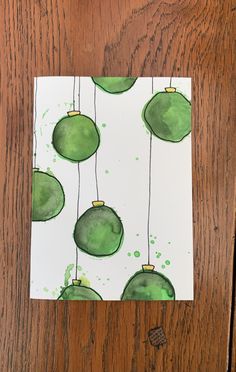 a piece of paper with green ornaments hanging from it's sides on a wooden surface