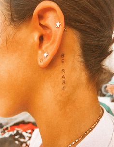 a woman with ear piercings that says be brave on her left side behind the ear