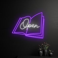 an open book neon sign on the wall next to a vase with flowers in it