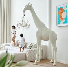 two girls are standing next to a giraffe statue in a living room with chandelier