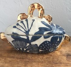 an ornate blue and white bowl with gold handles on a wooden table next to a wall