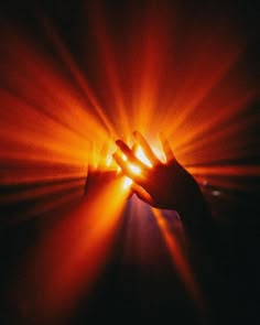 a person holding their hands up in the air with bright light coming from behind them