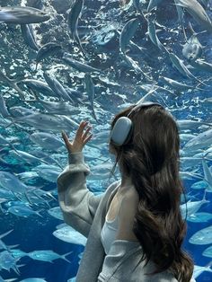 a woman wearing headphones standing in front of a large aquarium filled with lots of fish