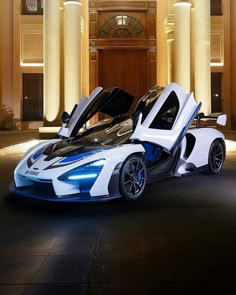 a white and blue sports car parked in front of a building at night with its doors open