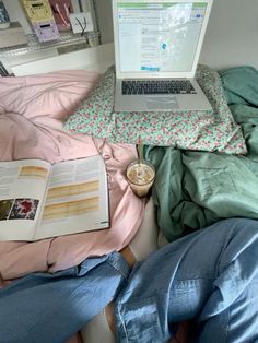 an open laptop computer sitting on top of a bed next to a book and cup