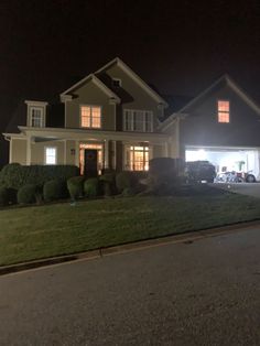 a house is lit up at night with the lights on and cars parked in front