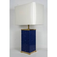 a blue and gold lamp with a white shade on the top, sitting against a white wall