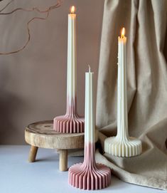 three candles sitting on top of a wooden table next to a drab cloth curtain