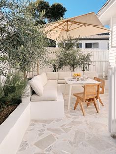 an outdoor living area with white furniture and umbrellas over the table, surrounded by greenery