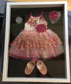 a pink and white dress with gold sequins in a shadow box next to shoes