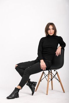 a woman sitting in a chair with her legs crossed and looking at the camera while wearing black