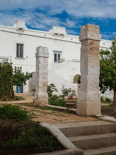 two stone pillars in front of a white building with trees and bushes on the side