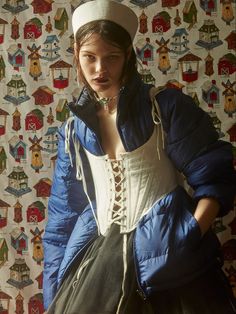 a woman in a blue jacket and white hat is posing for a photo with colorful wallpaper behind her