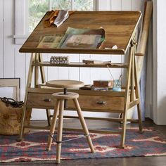 a wooden desk with drawers and stools in front of a white wall, next to a window