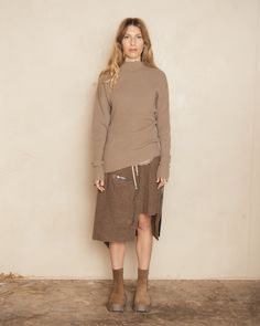 Dracca drawstring skirt by Rick Owens in fawn. Short skirt featuring a varied hemline, gracefully dipping from above the knee to a soft drape at the back. Adorned with two zipped Bauhaus pockets and a flap pocket at the rear, this skirt blends functionality with elegance. Crafted from textured brushed wool, it is woven in a fifth-generation Austrian mill, using only glacier water to achieve its luxurious finish. 100% Virgin Wool.Made in Italy. Pictured with Dust Dafne Knitted Wool Sweater and Du