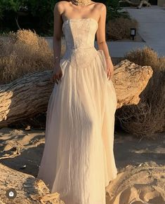 a woman standing on top of a sandy beach wearing a white dress and choker