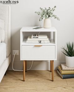 a white nightstand with books on it next to a potted plant and a bed