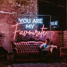 a man sitting on a couch in front of a neon sign that says you are my favorite