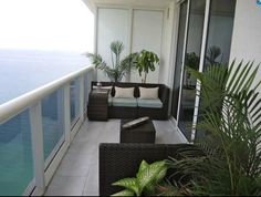 an outdoor balcony with wicker furniture and plants on the deck overlooking the ocean in front of it