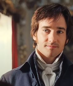 a man with long hair wearing a blue jacket and bow tie looking at the camera