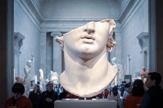 a group of people standing around a bust of a man in a museum like setting