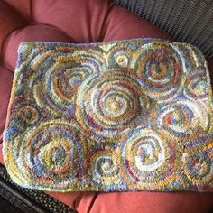 a crocheted rug sitting on top of a red cushion next to a wicker chair