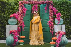 a woman standing in front of a green door wearing a yellow outfit with pink flowers