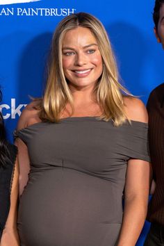 a pregnant woman standing next to two men in front of a blue wall and smiling