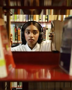 a woman with headphones on looking at the camera in front of bookshelves