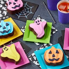 halloween treats are on colorful plates next to purple cups