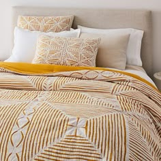 a bed with yellow and white pillows on top of it next to a night stand