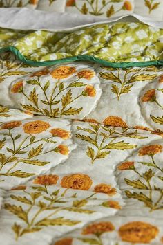 an unmade bed with yellow flowers and green trimmings on the comforter